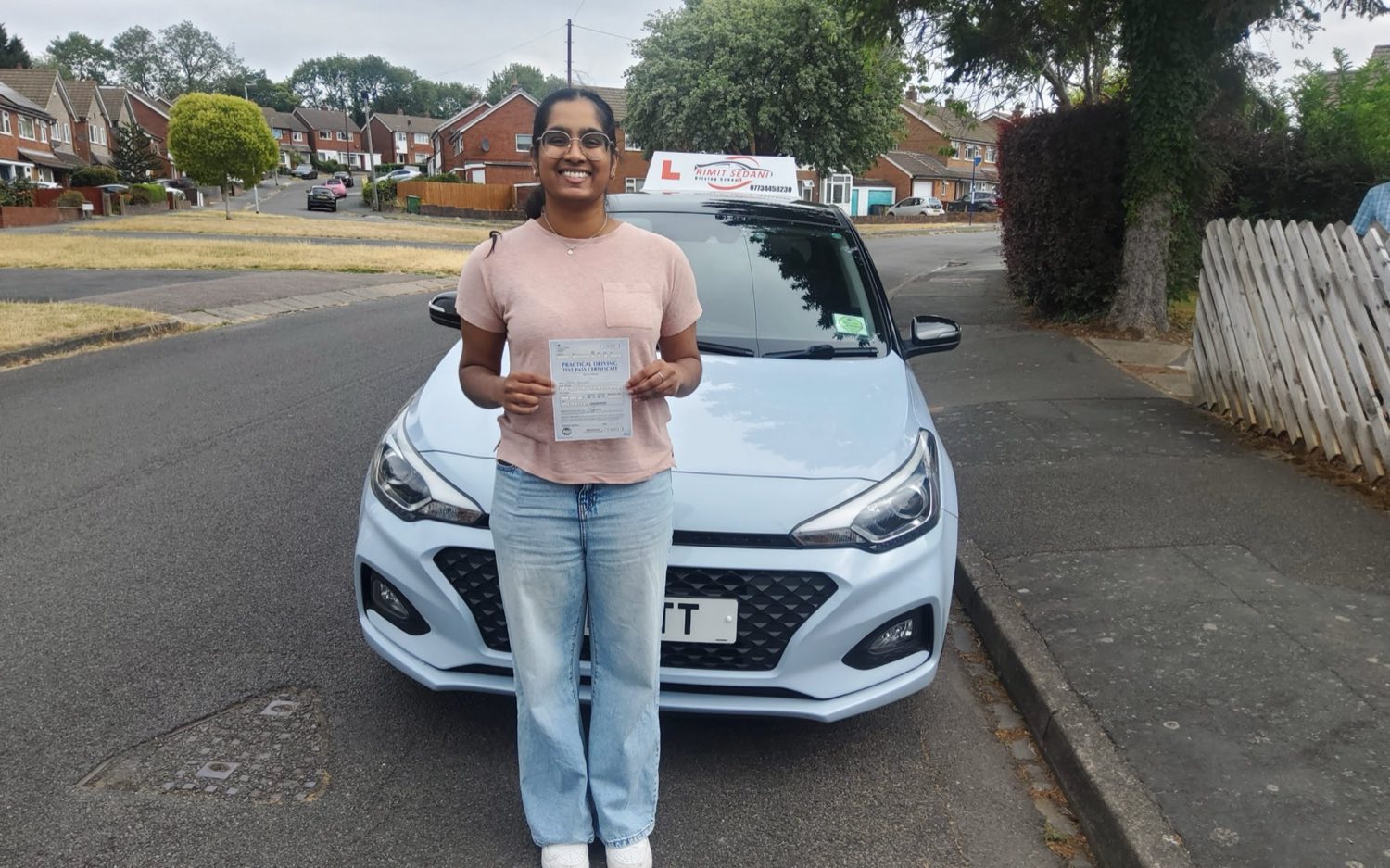 A learner holding her practical driving test pass certificate in front of the Rimit Sedani driving school car
